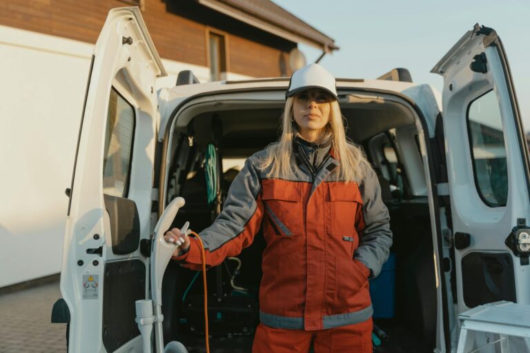 Female worker in uniform standing by a cleaning service van outdoors during the day.
